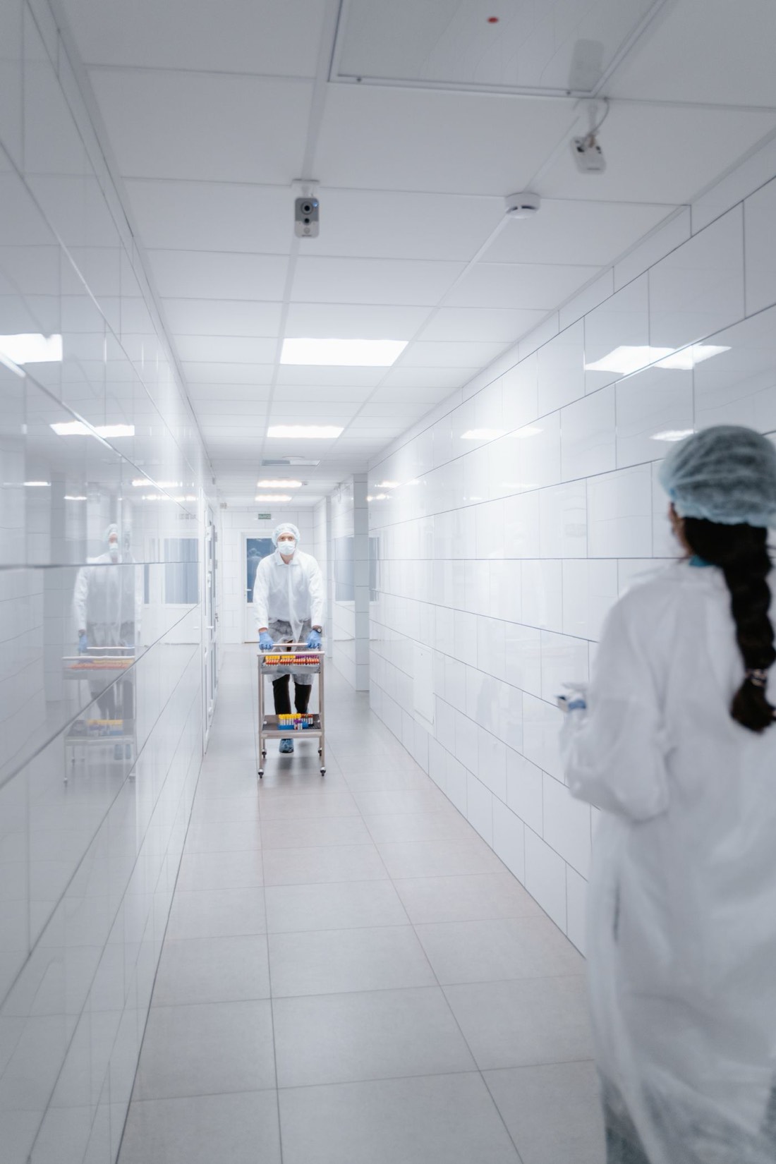 Staff in protective gowns moving between suites in a sterile pharmaceutical corridor